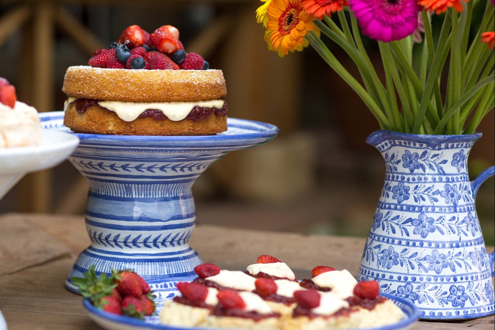 Dessert table with cake, fruit tart, and flowers in a vase.