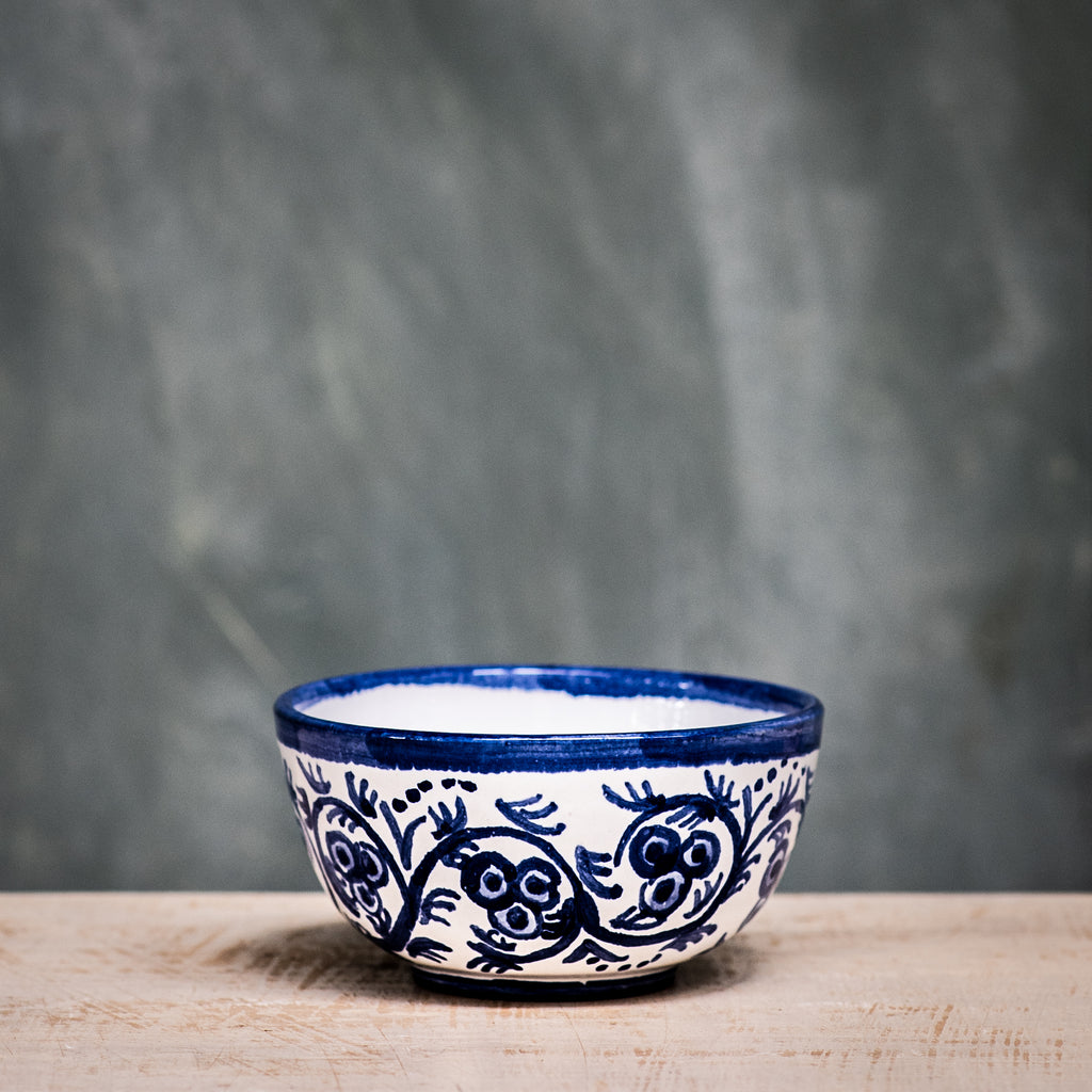 A blue and white floral patterned ceramic olive bowl placed on a wooden surface with a grey background.