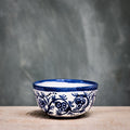 A blue and white floral patterned ceramic olive bowl placed on a wooden surface with a grey background.