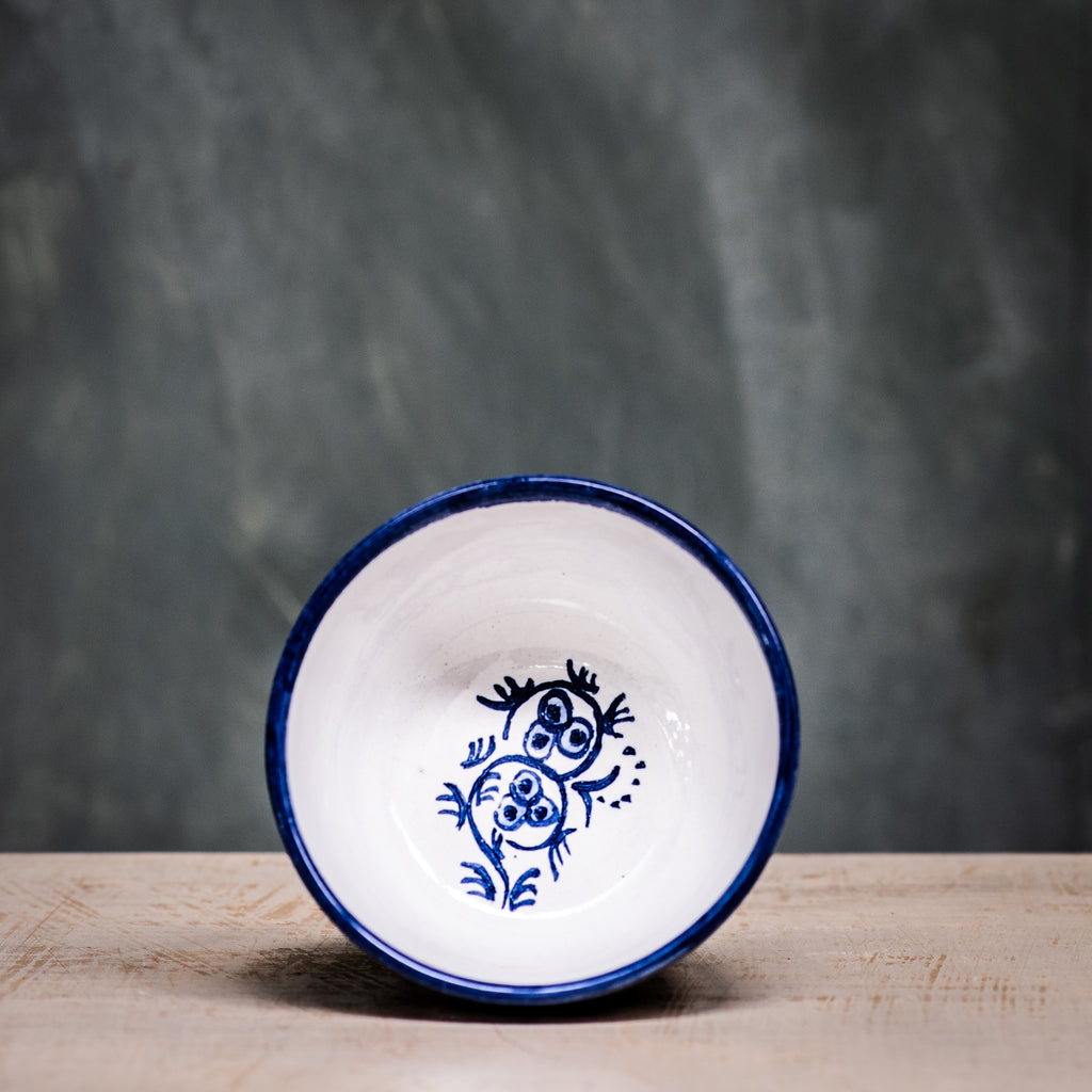A blue and white floral patterned ceramic olive bowl placed on a wooden surface with a grey background.