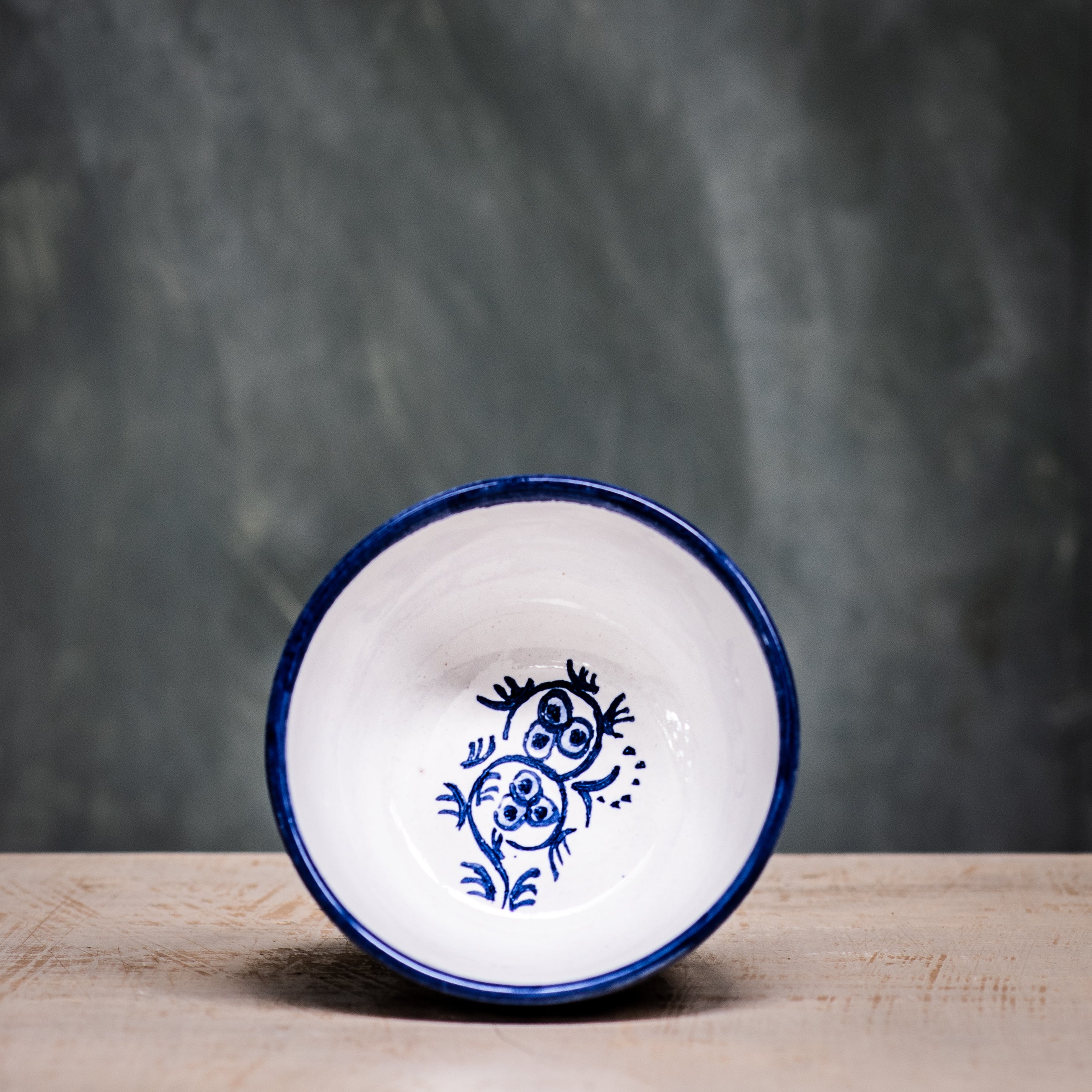 A blue and white floral patterned ceramic olive bowl placed on a wooden surface with a grey background.