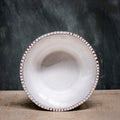 A white ceramic soup bowl with ridges  around the edge on a wooden surface with a blurred green background.