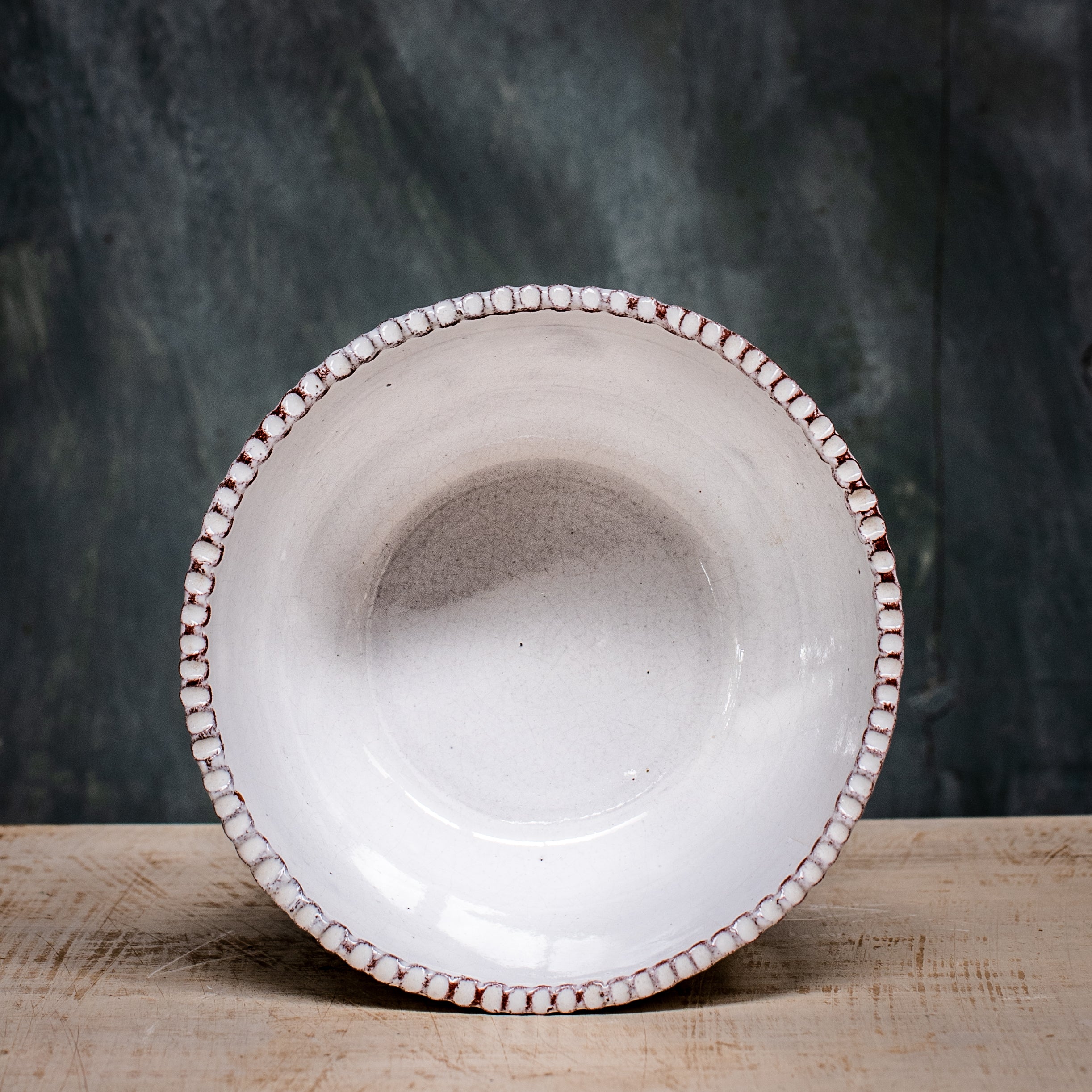 A white ceramic soup bowl with ridges  around the edge on a wooden surface with a blurred green background.