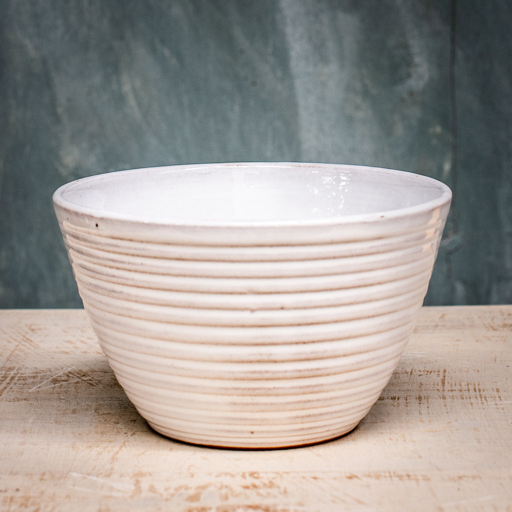A white ceramic pudding bowl with ridges on a wooden surface against a gray background.