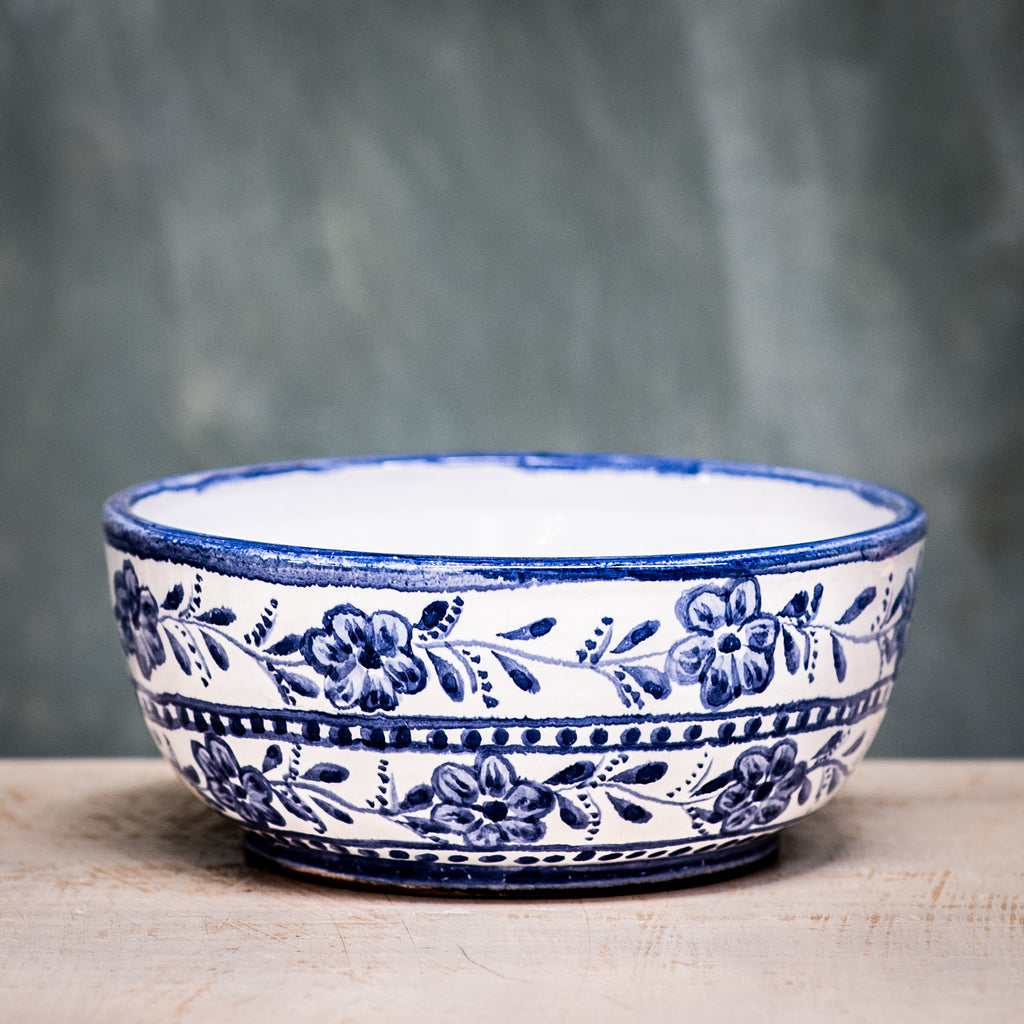 A blue and white floral patterned ceramic cereal bowl on a wooden surface with a plain green background.