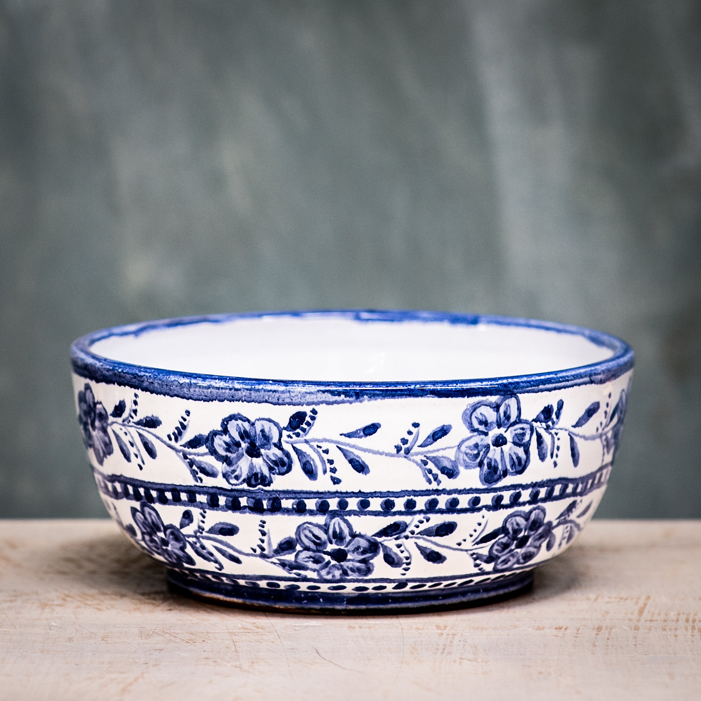 A blue and white floral patterned ceramic cereal bowl on a wooden surface with a plain green background.