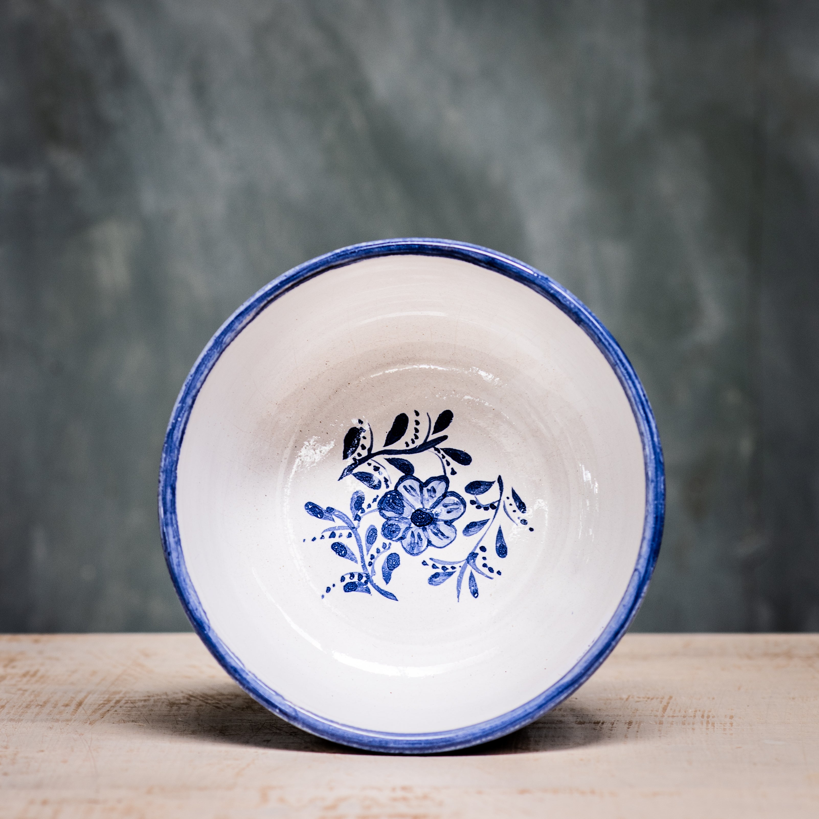 A blue and white floral patterned ceramic cereal bowl on a wooden surface with a plain green background.
