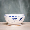 A ceramic cereal bowl with a white base and blue floral pattern on the side, placed against a grey background.