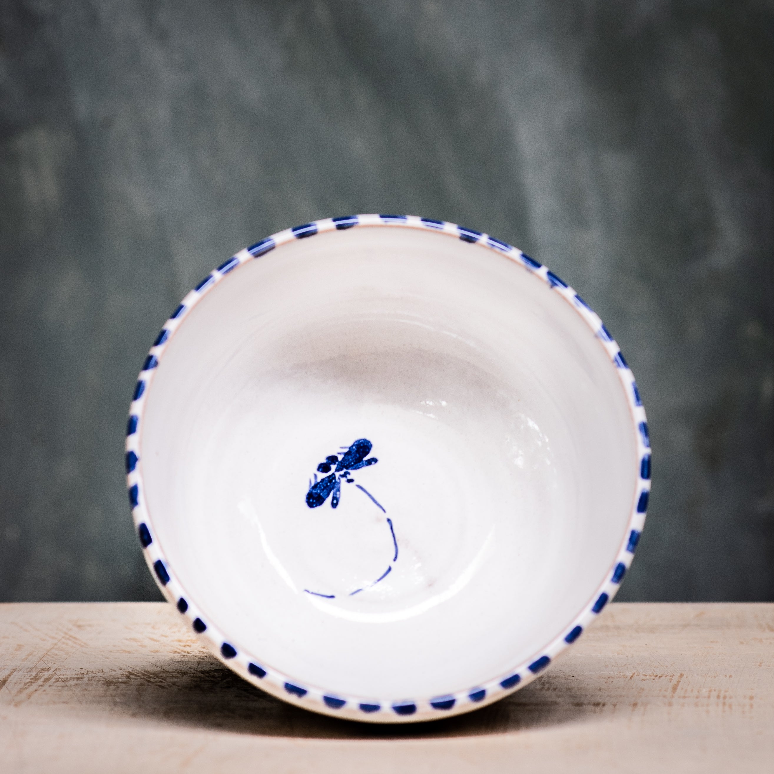 A ceramic cereal bowl with a white base and blue floral pattern on the side, placed against a grey background.