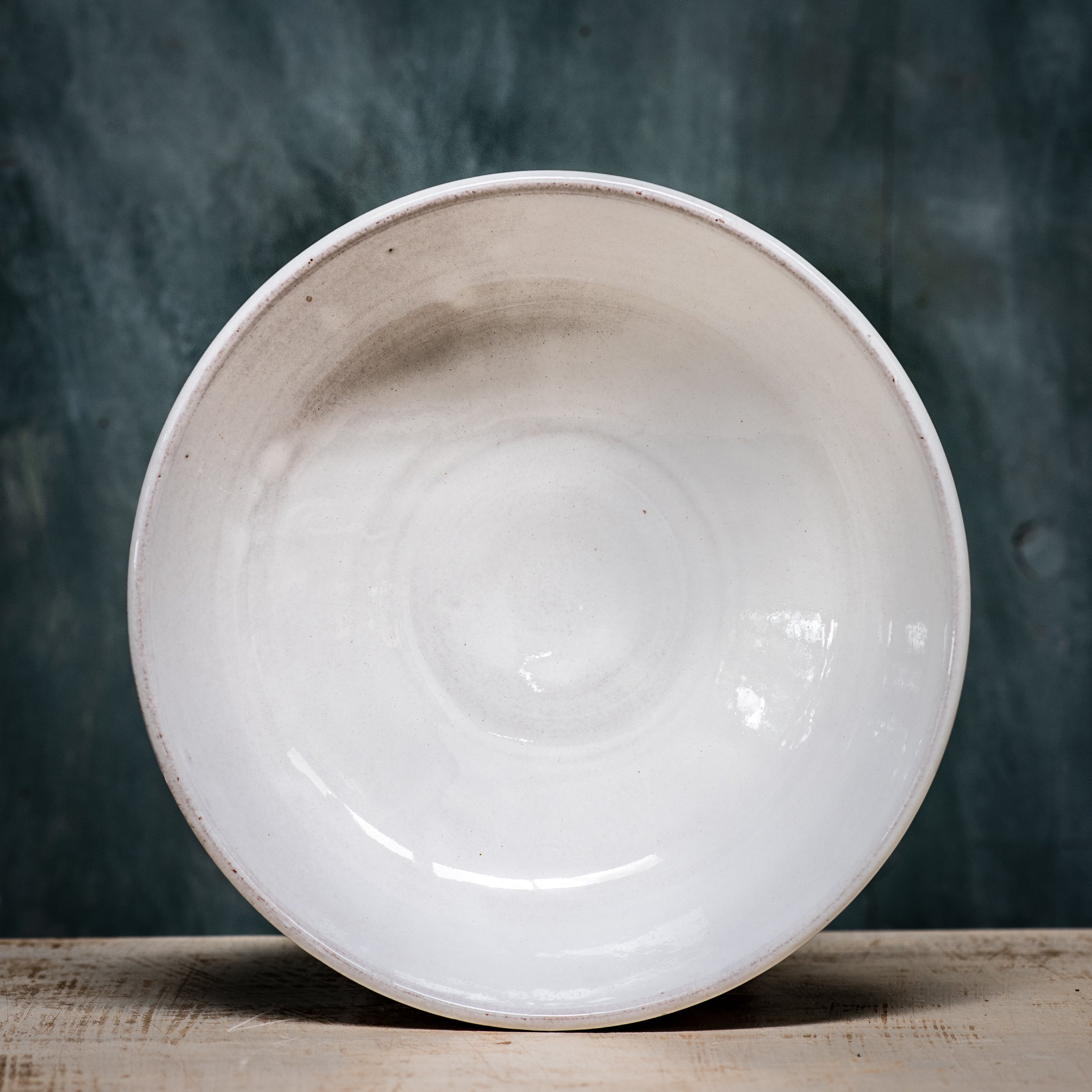 A white ceramic pasta bowl with a shallow design, displayed against a textured green background.