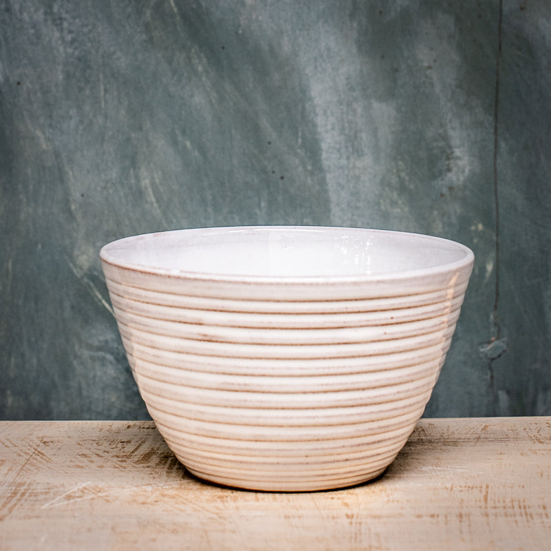 A white ceramic pudding bowl with ridges on a wooden surface against a gray background.