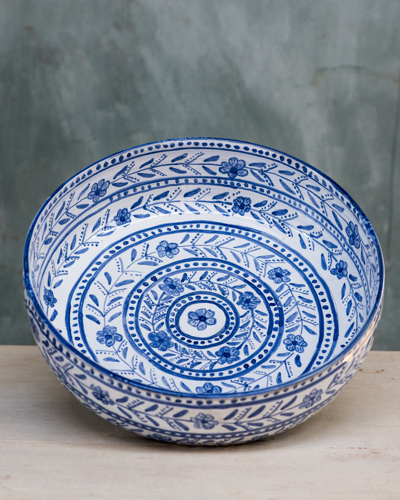 A shallow, round salad bowl with a blue and white floral pattern on it, displayed on a table.